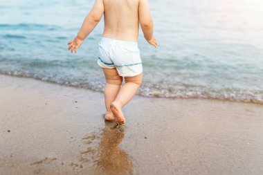 Geriye bakış sevimli sevimli sevimli yalnız beyaz çocuk yüzme şortlu mavi berrak su dalgalarında yürüyor tropikal deniz veya okyanus sahillerinde. Tatil ve küçük çocuk konseptiyle seyahat