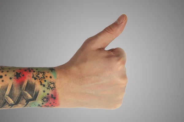 La mano de un hombre con un tatuaje muestra el símbolo sobre un fondo gris . — Foto de Stock