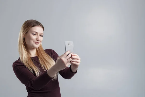 Het meisje maakt selfie op de telefoon op een grijze achtergrond, isoleren — Stockfoto