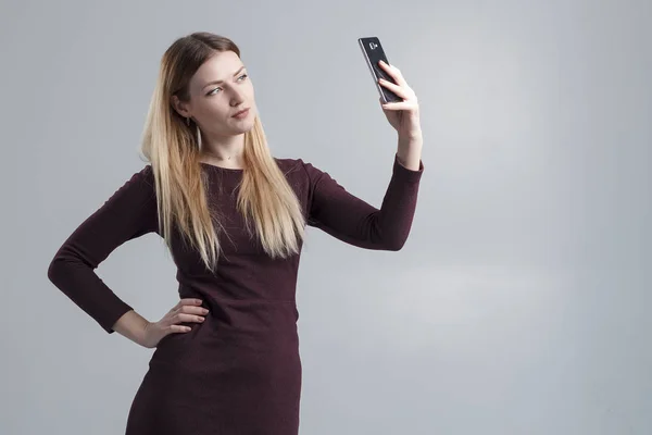 Het meisje maakt selfie op de telefoon op een grijze achtergrond, isoleren — Stockfoto