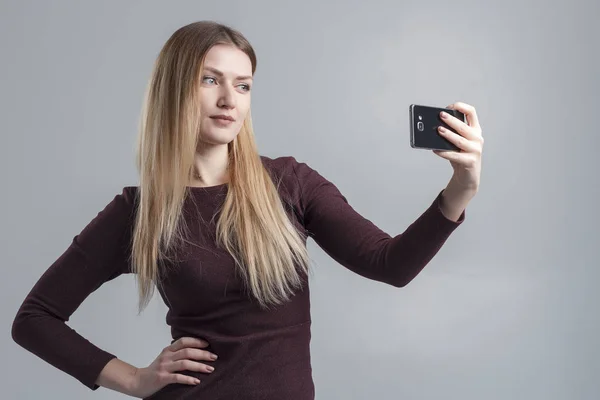 Het meisje maakt selfie op de telefoon op een grijze achtergrond, isoleren — Stockfoto