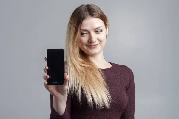 Close-up van portret van een lachende vrouw tonen scherm mobiele telefoon terwijl permanent geïsoleerde over grijze achtergrond — Stockfoto