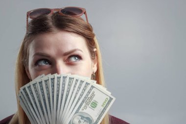 Bordo bir kazak, bir kız yüzünü yüz dolarlık banknot ile kapsar.