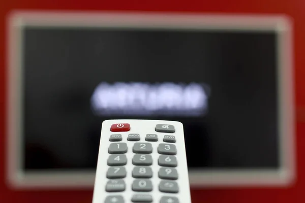 Пульт в руке переключает каналы на телевизоре, висящем на красной стене — стоковое фото