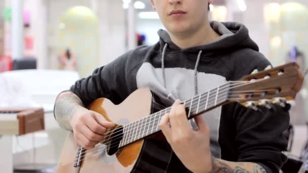 El tipo toca una guitarra clásica en una tienda de música, un ambiente musical, música clásica — Vídeo de stock