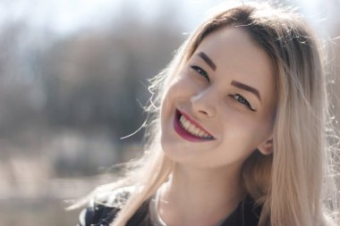 Güzel esmer bir kızın açık hava portresi. Güneşli yaz ya da bahar gününde şehrin arka planında mutlu gülümseyen bir kadın. Altın saat içinde yakın plan bir portre. Seçici odak.