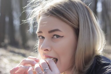 Kıvırcık saçlı genç bir kız açık havada güneşli bir günde pozlar..