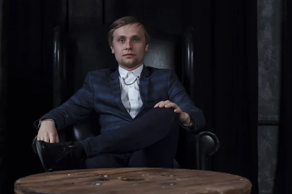 Handsome attractive elegant classic man wearing trendy suit, with beard, sitting and having rest on luxury furniture in fashionable dark interior A man in an expensive suit on the background of an exp