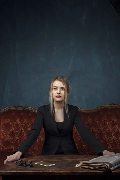 Retrato de uma mulher bonita em um terno preto que olha diretamente para a câmera em um interior antigo caro contra um fundo de parede texturizado azul com espaço para texto. Senhora de negócios, um sucesso — Fotografia de Stock