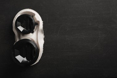 İki adet tek kullanımlık kahve bardağı ve siyah ahşap arka planda tek kullanımlık bardak tutacağı. Üst Manzara. Konsept: yemek teslimatı. Paket servis. Kahve hazır..