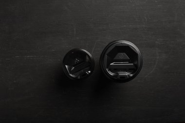 Siyah ahşap arka planda iki farklı boyutta tek kullanımlık kahve bardağı. Üst Manzara. Konsept: yemek teslimatı. Paket servis. Kahve hazır..