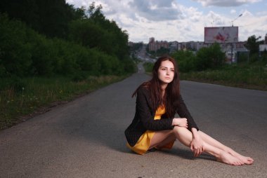 Genç esmer kız bir şehirde yerde oturuyor.