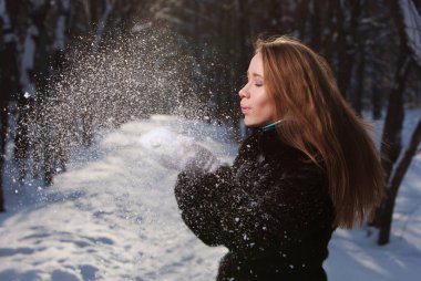 Kız parkta karla oynuyor. Kar ormanlarını uçuruyor.