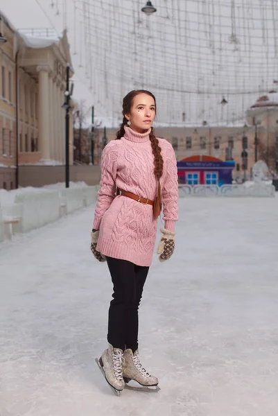 若いです可愛いです女性の服を着てピンクのスウェットシャツ上の氷の上に立ってスケート 屋外アイススケートリンク — ストック写真