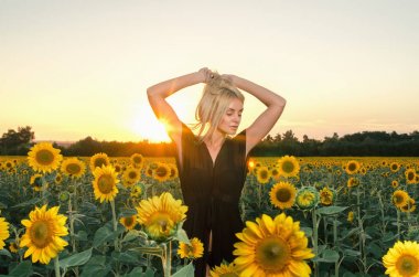 Ayçiçeği tarlası üzerinde siyah elbiseli güzel genç sarışın model