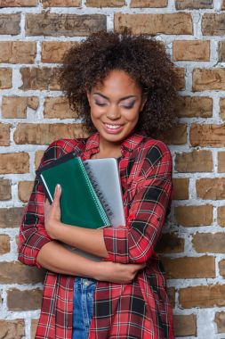 laptop ve defter tutarken gülümseyen şık Afro-Amerikan kız