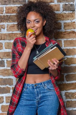 Afro-Amerikan kız yeme elma ve kameraya ararken holding Notebook