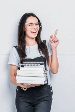 young caucasian student holding books and pointing with finger