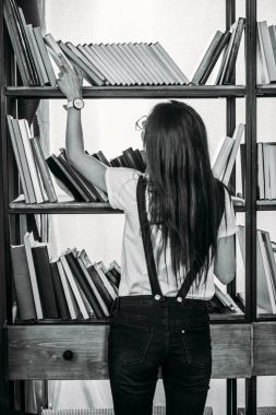 Raflardan duran ve kitap seçimi genç kadın fotoğrafı siyah-beyaz