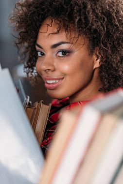 Kitap tutan ve kameraya gülümseyen çekici genç Afro-Amerikan öğrenci 