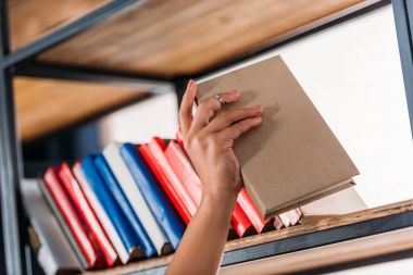 Öğrenci kitap kütüphane içinde bookshelf de tutarak atış kırpılmış 