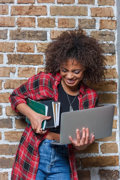 Ung snygg kvinna leende medan du håller laptop och anteckningsböcker — Gratis stockfoto