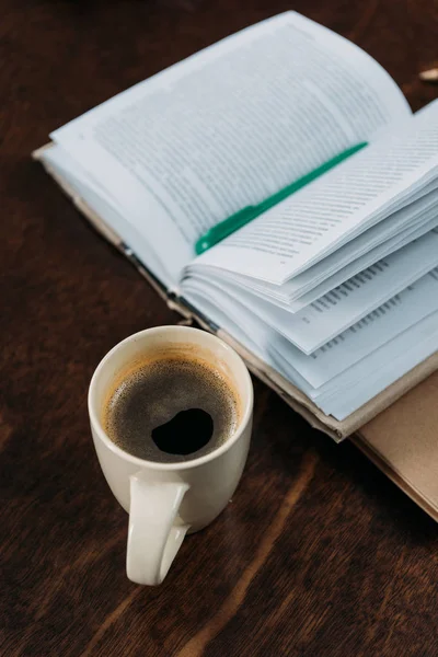 Close up of coffee cup with book and pen on wooden tabletop — Stock Photo, Image