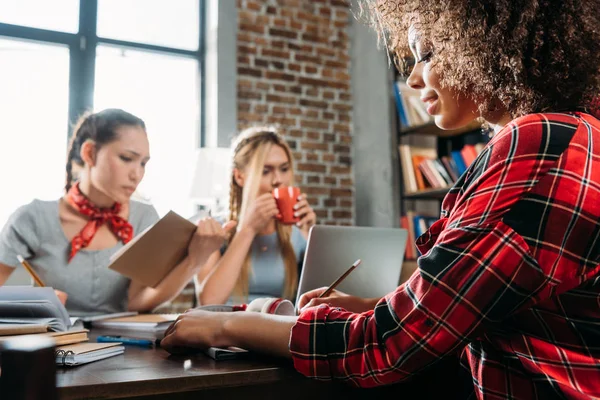 Mulheres multiétnicas jovens que trabalham enquanto se sentam à mesa no escritório em casa — Fotografia de Stock