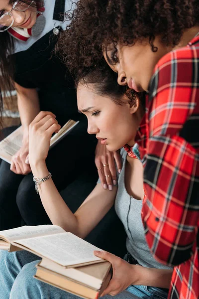 Jovem chateado mulheres multiétnicas abraçando e segurando livros — Fotografia de Stock