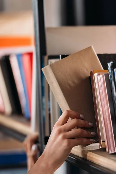 Schnappschuss von Studentin, die Buch im Bücherregal in Bibliothek hält — Stockfoto