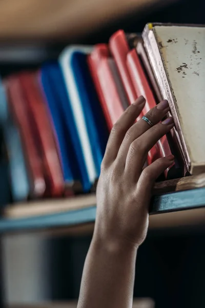 Обрізаний знімок студентського тримання книги на книжковій полиці в бібліотеці — стокове фото