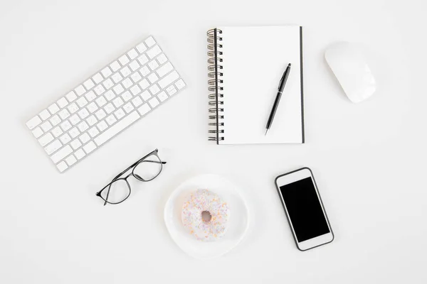 顶视图的空白屏幕智能手机、 笔、 眼镜、 键盘、 电脑鼠标与美味甜甜圈的工作场所的空白笔记本 — 图库照片