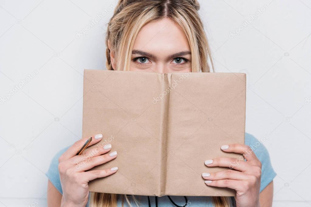 young blonde woman holding book in front of face and looking at camera