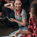 Atractivas mujeres jóvenes con teléfono inteligente y taza de café sonriendo entre sí