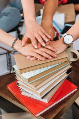 Close-up view of young women stacking hands on pile of books