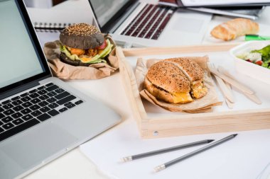 tasty burgers with fresh salad and bread loaf with laptops on tabletop clipart