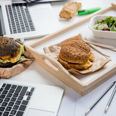 close up of tasty burgers with fresh salad and bread loaf with laptops on tabletop clipart