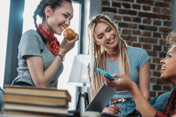 Улыбающиеся молодые женщины с яблоком и смартфоном разговаривают и смотрят друг на друга — стоковое фото