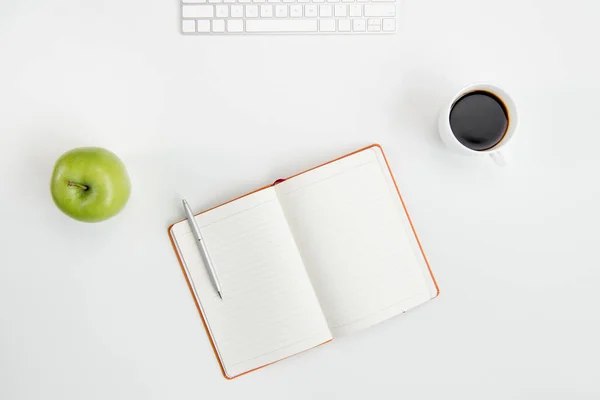 Vue du dessus du bloc-notes ouvert vierge avec stylo, tasse de café, pomme verte et clavier sur le lieu de travail — Photo
