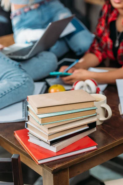Close-up view of pile of books on wooden table and young friends sitting behind — Stock Photo, Image