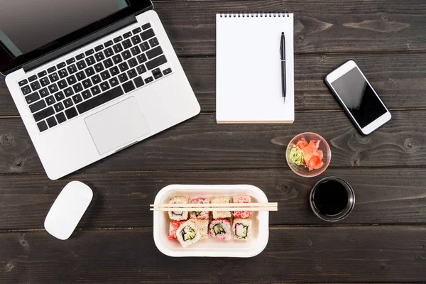 Vedere de sus a laptopului cu mouse-ul computerului, notebook-ul gol cu stilou, smartphone și sushi setat pe masă din lemn — Fotografie, imagine de stoc