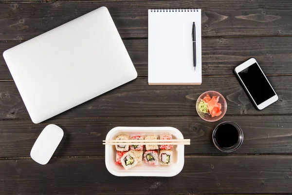 Vista superior de la computadora portátil con el ratón de la computadora, portátil en blanco con pluma, teléfono inteligente y sushi establecido en la mesa de madera — Foto de Stock