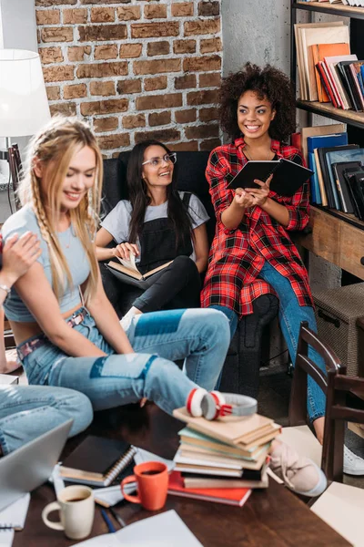 Mujeres jóvenes sonrientes sentadas y estudiando junto con libros — Foto de Stock