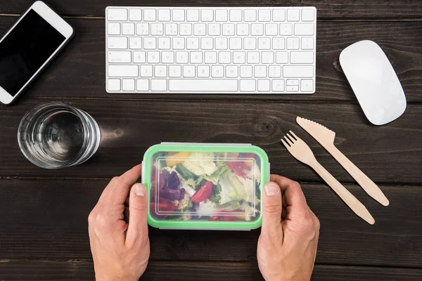 Vista superior del lugar de trabajo con dispositivos digitales y manos humanas capaces de comer ensalada durante el trabajo — Foto de Stock