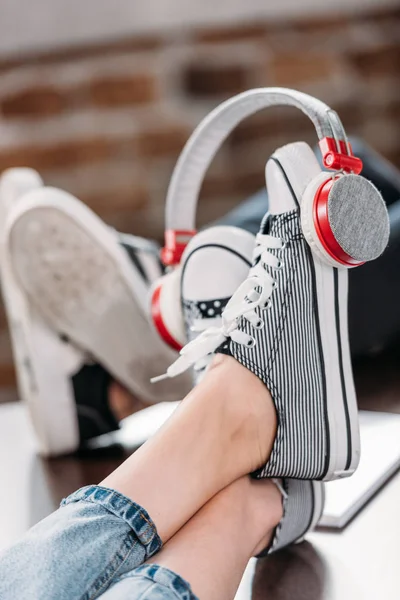 Pandangan dekat kaki perempuan dengan sepatu bergaya dengan headphone di atas meja kayu — Stok Foto