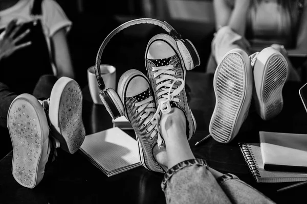 Vista de perto dos pés da mulher em sapatos elegantes com fones de ouvido na mesa de madeira, foto em preto e branco — Fotografia de Stock