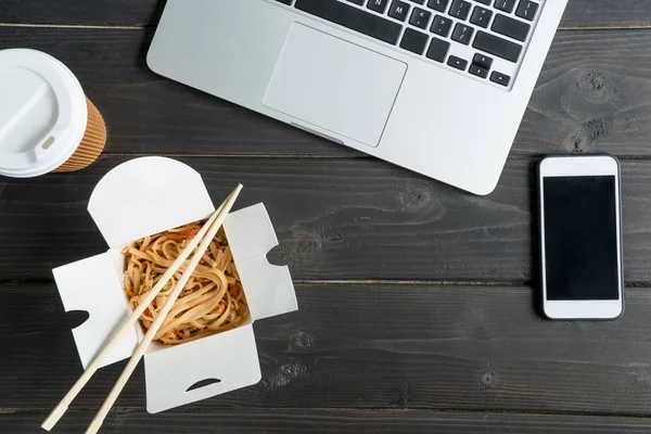 Vista superior de macarrão com pauzinhos e laptop com café para ir em mesa de madeira — Fotografia de Stock
