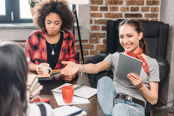 Atractivos jóvenes amigos tomando café y estudiando junto con libros y tabletas digitales —  Fotos de Stock