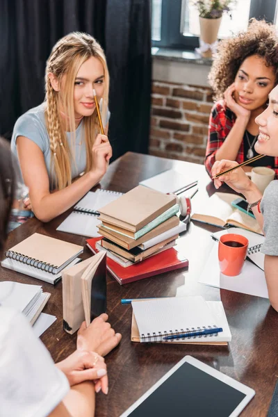 Hermosas mujeres jóvenes sentadas juntas en la mesa y estudiando con libros y cuadernos —  Fotos de Stock