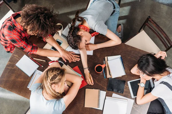 Overhead view of tired young students sleeping on table with notebooks and digital devices — Stock Photo, Image